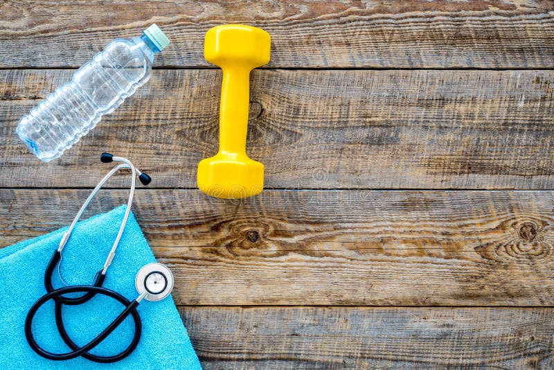 Sport and health. Fitness. Dumbbells and stethoscope on wooden background top view copyspace