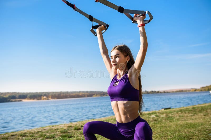 Sport woman doing  training outdoors with TRX at daytime. Total body resistance exercises for her healhty lifestyle