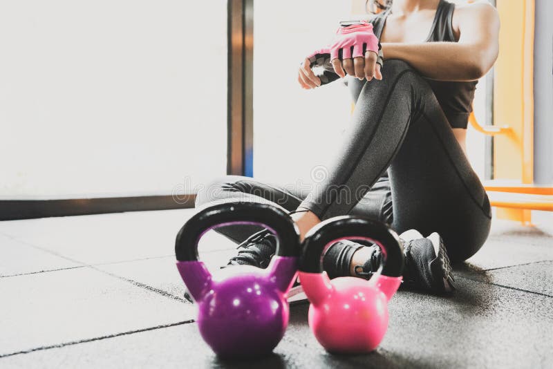 Sport woman sitting and resting after workout or exercise in fitness gym with protein shake or drinking water on floor. Relax conc