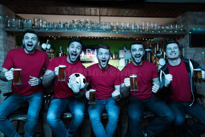 Sportfans som framme firar och hurrar av tv som dricker öl på sportstången fotografering för bildbyråer Sportfans som framme firar och hurrar av tv som dricker öl på sportstången fotografering för bildbyråer