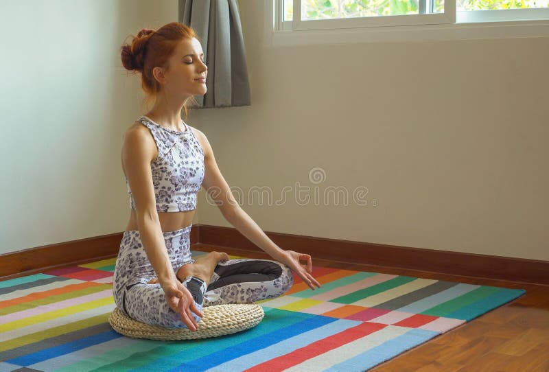 Sportieve jonge vrouw die yogapraktijk in de lotusbloempositie doen inzake mat in huis, de training van het geschiktheidsmeisje i royalty-vrije stock afbeelding Sportieve jonge vrouw die yogapraktijk in de lotusbloempositie doen inzake mat in huis, de training van het geschiktheidsmeisje i royalty-vrije stock afbeelding