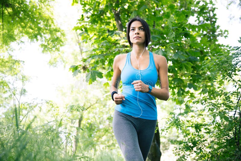 Sportieve vrouw in hoofdtelefoons die in openlucht lopen stock afbeelding Sportieve vrouw in hoofdtelefoons die in openlucht lopen stock afbeelding
