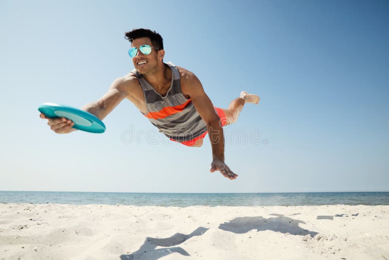 Sportive Man Jumping and Catching Flying Disk at Beach Stock Image