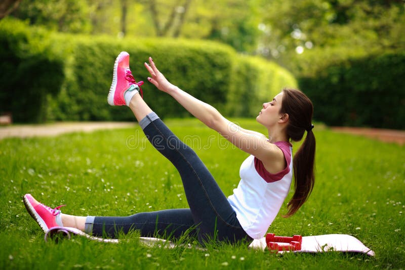 Sportive young woman stretching, doing fitness exercises in park