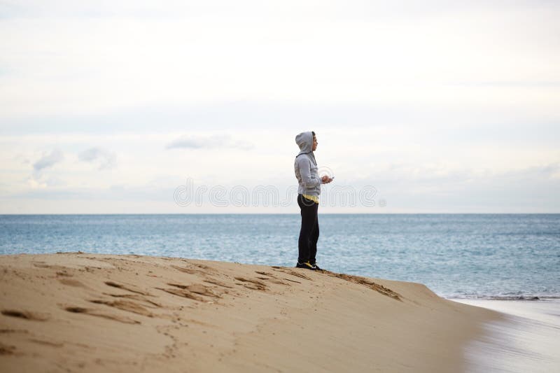 Sportlicher junger Mann, der auf dem Strand beim Machen der Pause während des Trainings steht lizenzfreies stockfoto Sportlicher junger Mann, der auf dem Strand beim Machen der Pause während des Trainings steht lizenzfreies stockfoto