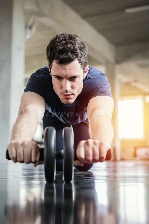 Sportlicher Mann des Athleten, der ?bung mit ABSrollenrad tut, um seinen Bauchmuskel in der Turnhalle zu verst?rken stockbild Sportlicher Mann des Athleten, der ?bung mit ABSrollenrad tut, um seinen Bauchmuskel in der Turnhalle zu verst?rken stockbild