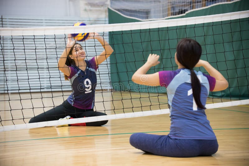 Sports for disabled people. Two young women sitting on the floor and playing volleyball. Smiling stock photos Sports for disabled people. Two young women sitting on the floor and playing volleyball. Smiling stock photos