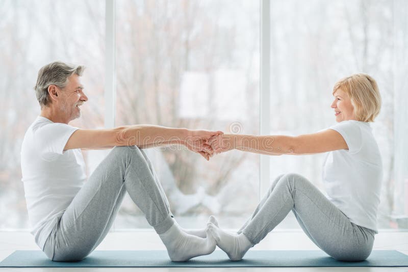 Sports and healthy lifestyle.Sporty middle aged couple sitting on the mat in the white fitness gym and doing stretching while