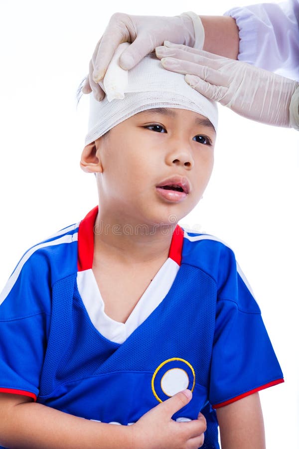 Sports injury. Athlete little asian (thai) boy in blue sportswear with trauma of the head. Doctor makes a bandage on head patient. Child unhappy, on white background. Studio shoot. Sports injury. Athlete little asian (thai) boy in blue sportswear with trauma of the head. Doctor makes a bandage on head patient. Child unhappy, on white background. Studio shoot.