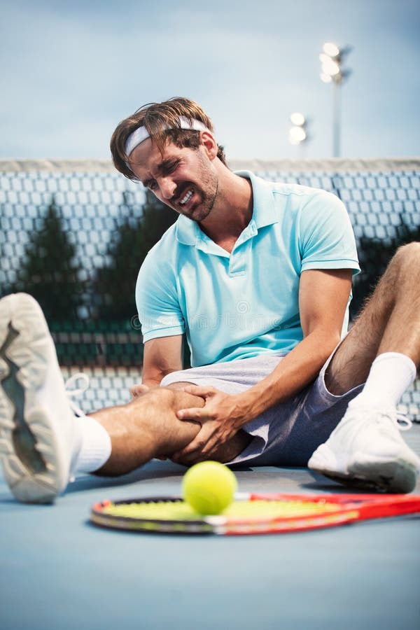 Sports injury. Young tennis player touching his knee while sitting on the tennis court