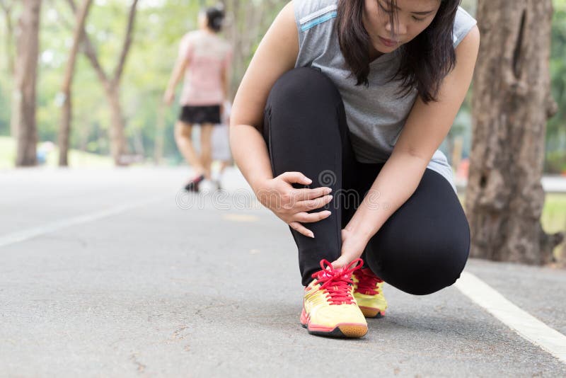 Sports injury. Woman with pain in ankle while jogging in park