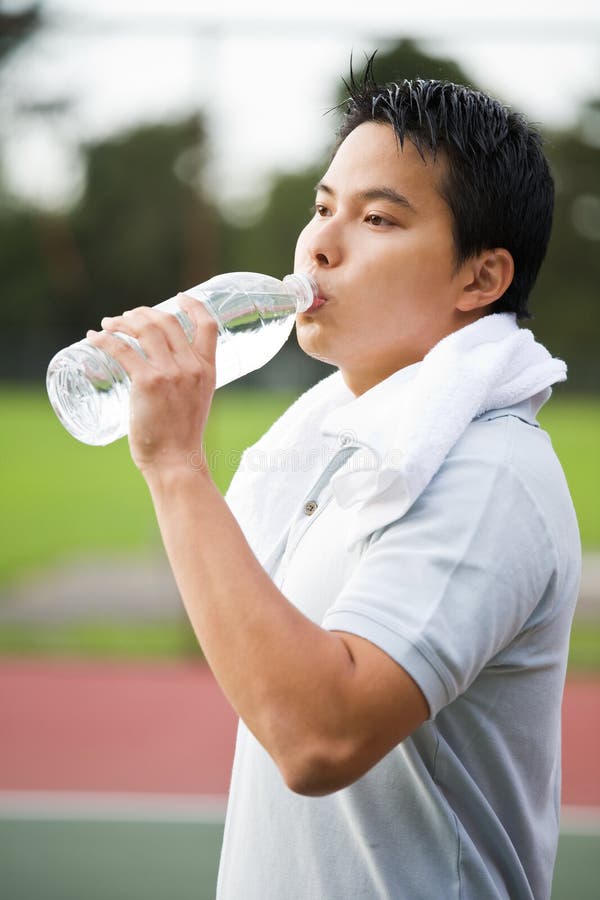 A young sporty active asian male drinking water after exercise. A young sporty active asian male drinking water after exercise