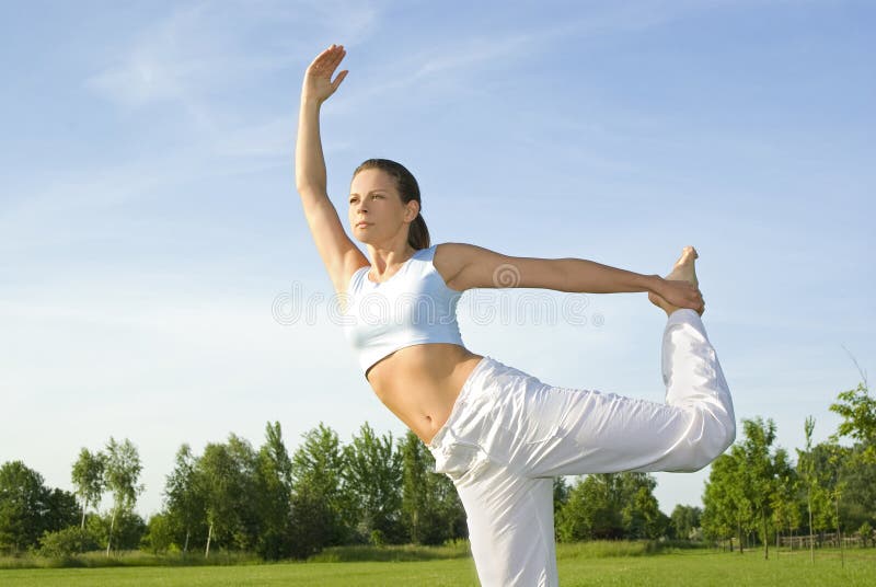 Sporty girl exercising on meadow against the sky