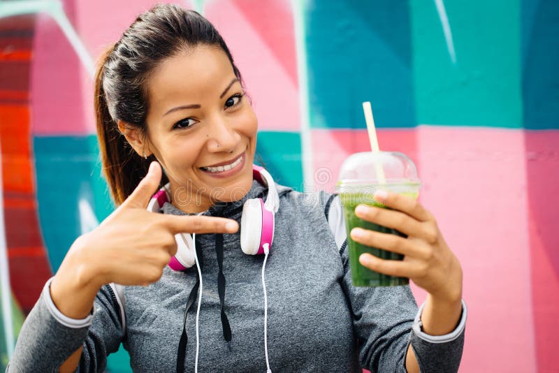 Successful fitness urban woman taking a rest for drinking and recommending detox smoothie. Healthy nutrition and lifestyle concept. Successful fitness urban woman taking a rest for drinking and recommending detox smoothie. Healthy nutrition and lifestyle concept.