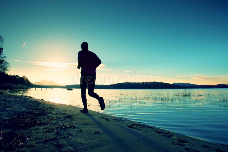 Sporty Man doing Morning Jogging on Sea Beach at Bright Sunrise Silhouettes