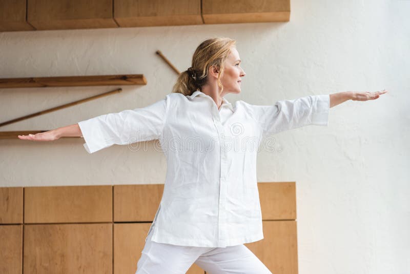 sporty mature woman performing warrior pose while practicing yoga