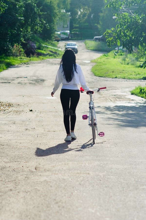 Sporty tjej går med cykel planera tillbaka Snygg friskhetsflicka med sportcykelpromenader i parken Strålningskompetens arkivfoton