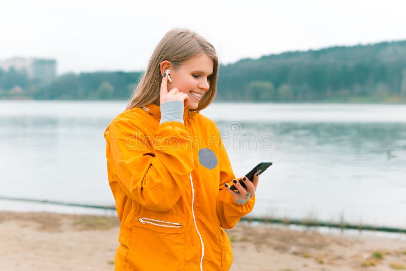 Sporty woman is walking and using her earpods and phone near a forest lake.