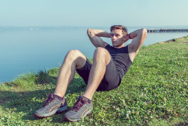 Sporty Young Man Doing Situps Abs Crunches in Nature. Stock Photo