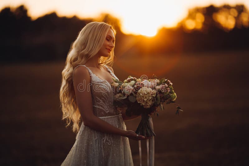 Sposa romantica che tiene il boquet di nozze, posante al tempo di tramonto immagini stock libere da diritti Sposa romantica che tiene il boquet di nozze, posante al tempo di tramonto immagini stock libere da diritti