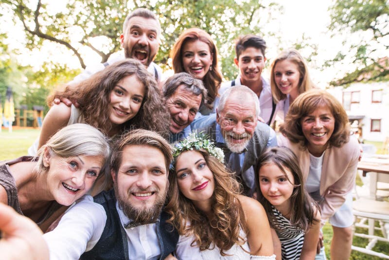Sposa, sposo con gli ospiti che prendono selfie al ricevimento nuziale fuori nel cortile