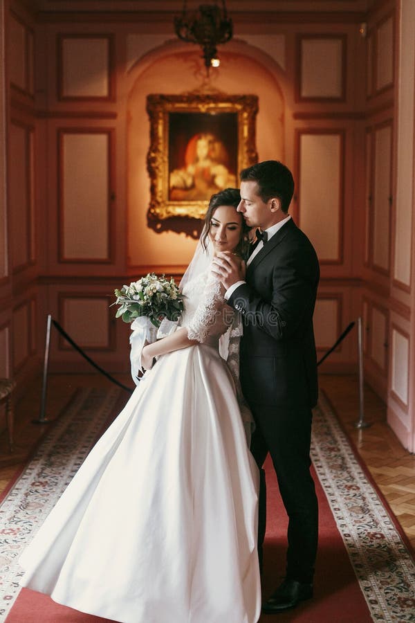 Gorgeous bride and stylish groom hugging in luxury room in hotel. rich wedding couple embracing. romantic moment of newlyweds in amazing classic interior. Gorgeous bride and stylish groom hugging in luxury room in hotel. rich wedding couple embracing. romantic moment of newlyweds in amazing classic interior