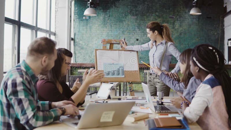 Meeting of mixed race business team at loft office. Woman manager presenting financial data, group of people clapping. Team leader presentation project and financial data to her colleagues. Meeting of mixed race business team at loft office. Woman manager presenting financial data, group of people clapping. Team leader presentation project and financial data to her colleagues.