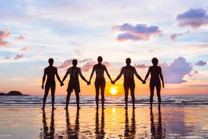 Community or group concept, silhouettes of people standing together and holding hands, team on the beach, unity background. Community or group concept, silhouettes of people standing together and holding hands, team on the beach, unity background