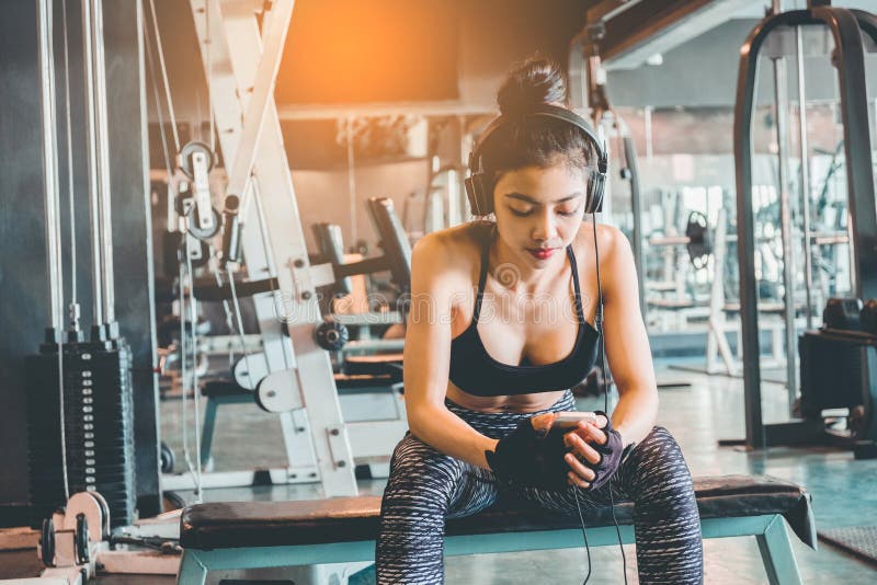 Sprawności fizycznej dziewczyna używa smartphone i hełmofony w sprawności fizycznej gym obraz stock Sprawności fizycznej dziewczyna używa smartphone i hełmofony w sprawności fizycznej gym obraz stock