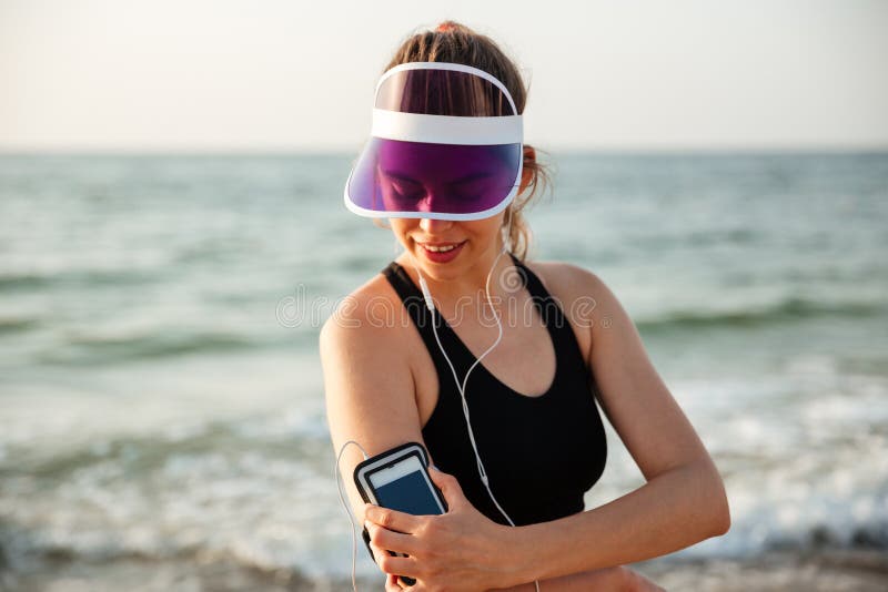 Sprawności fizycznej kobieta odpoczywa na plażowym słuchaniu muzyka z telefonem zdjęcia stock Sprawności fizycznej kobieta odpoczywa na plażowym słuchaniu muzyka z telefonem zdjęcia stock