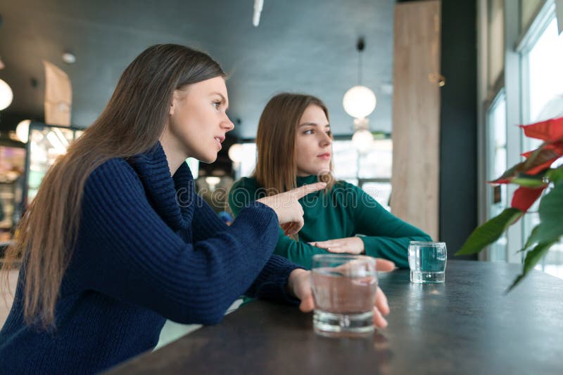 Sprechende junge Frauen, Mädchen, die im Café lächelnd und sprechend, trinkendes Trinkwasser im Glas, das Fenster heraus schauend stockfotografie Sprechende junge Frauen, Mädchen, die im Café lächelnd und sprechend, trinkendes Trinkwasser im Glas, das Fenster heraus schauend stockfotografie