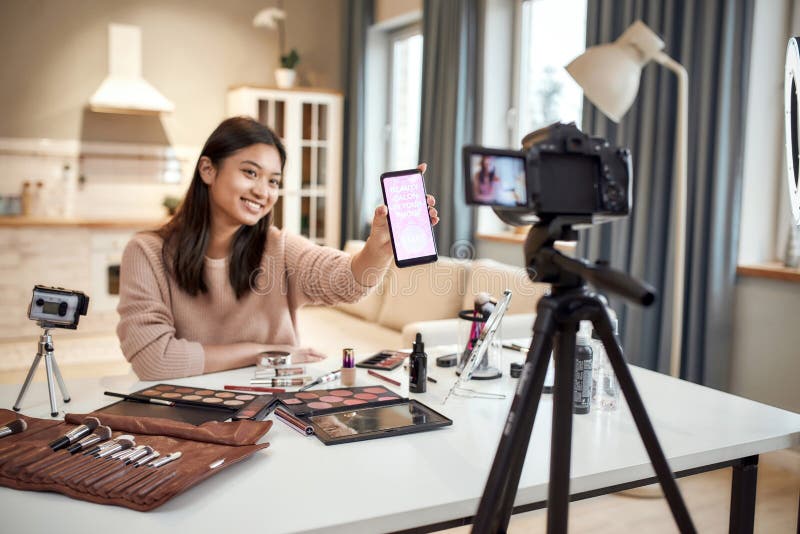 Sprida din charm. skönhetsbloggare, kvinna som filmar reklamapp på kameran som håller smartphone. makeup influencer asian arkivbild