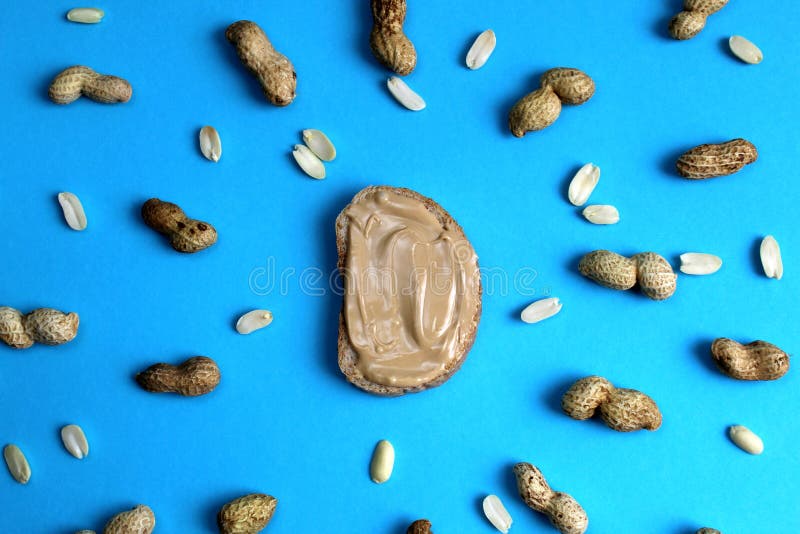 Spridning för jordnötsmör på ett stycke av bröd. Bröd jordnötsmör, spridning, jordnöt, skalat som är unpeeled, mat, smörgås, frukost, bröd, kräm, mutter, mellanmål, ingrediens som är smaklig, mat som är naturlig, protein, sötsak, hög-kalori, skiva, amerikan, efterrätt, textur, bakgrund, muttrar, kalorier, närbild,