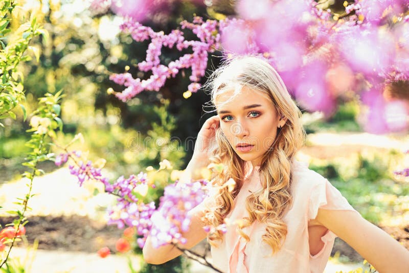 Spring bloom concept. Young woman enjoy flowers in garden, defocused. Girl on dreamy face, tender blonde near violet