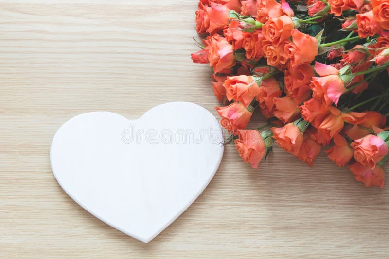 Spring concept. Bouquet of orange roses with white heart as blank on wooden board. Top view. Romantic or Valentine`s card. Copy s