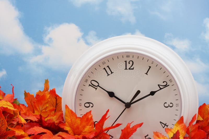 Spring Forward, Fall Back. White clock on fall leaves, sky background Spring Forward, Fall Back. White clock on fall leaves, sky background