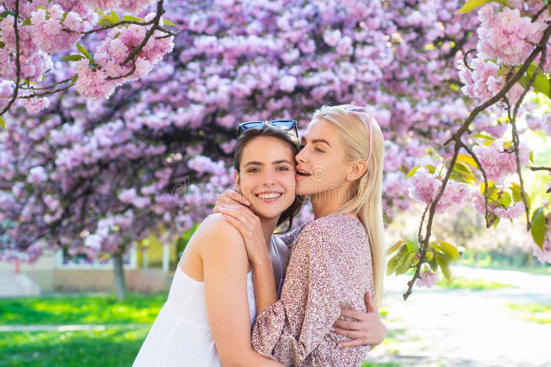 Spring girls in flowers. Outdoor portrait of young beautiful happy smiling female couple posing near flowering tree.