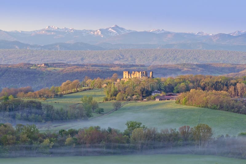 Ruins of Chateau Lagarde and the high french countryside. Lagarde Areige France 04.23.23 Spring time Panorama. Early morning mist drifts over green meadow lined