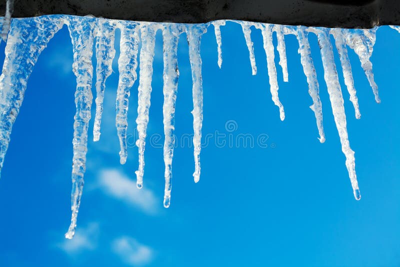 Spring landscape with ice icicles hanging from roof of house