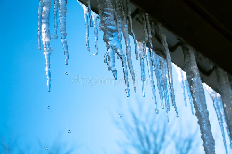 Spring landscape with ice icicles hanging from roof of house.