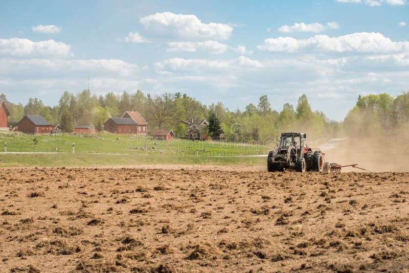 Ljusfallshammar, Sweden - May 9, 2016: Tractor pulling a plow during spring in the countryside between Finspång and Ljusfallshammar. Springtime in Sweden is fresh, green and flowering with long bright days. Ljusfallshammar, Sweden - May 9, 2016: Tractor pulling a plow during spring in the countryside between Finspång and Ljusfallshammar. Springtime in Sweden is fresh, green and flowering with long bright days.