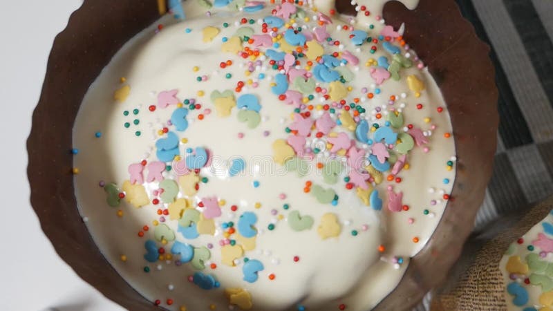 Sprinkle Easter cakes with sprinkles. On sweet glazed white Easter cakes pour rainbow splashes. Traditional preparation stock video footage