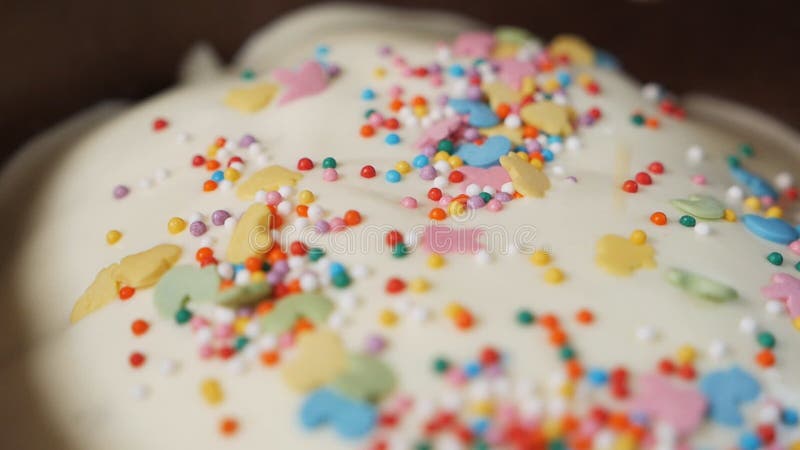 Sprinkle Easter cakes with sprinkles. On sweet glazed white Easter cakes pour rainbow splashes. Traditional preparation stock footage