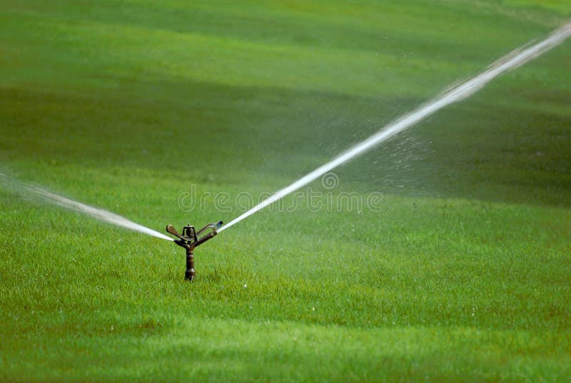 Sprinkler spraying stream of water on lush green grass. Sprinkler spraying stream of water on lush green grass