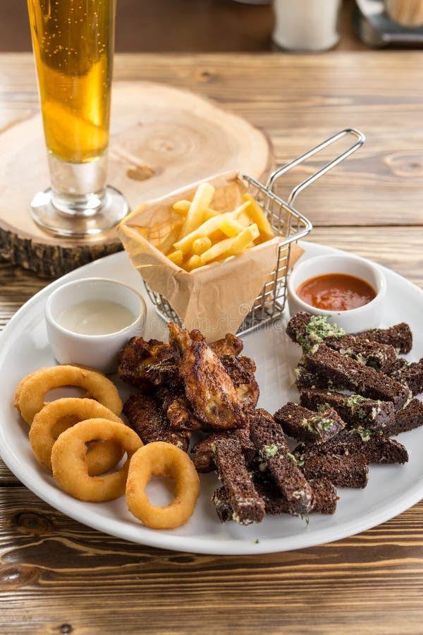 Spuntini ordinati come le ali di pollo, le patate fritte, il crostino del pane di segale ed il vetro di birra sulla tavola di leg immagine stock libera da diritti Spuntini ordinati come le ali di pollo, le patate fritte, il crostino del pane di segale ed il vetro di birra sulla tavola di leg immagine stock libera da diritti