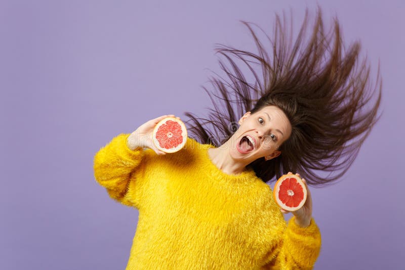 Spännande ung kvinna med flödande hår som håller öppna rymmande halfs för mun av den nya mogna grapefrukten som isoleras på viole royaltyfri foto Spännande ung kvinna med flödande hår som håller öppna rymmande halfs för mun av den nya mogna grapefrukten som isoleras på viole royaltyfri foto