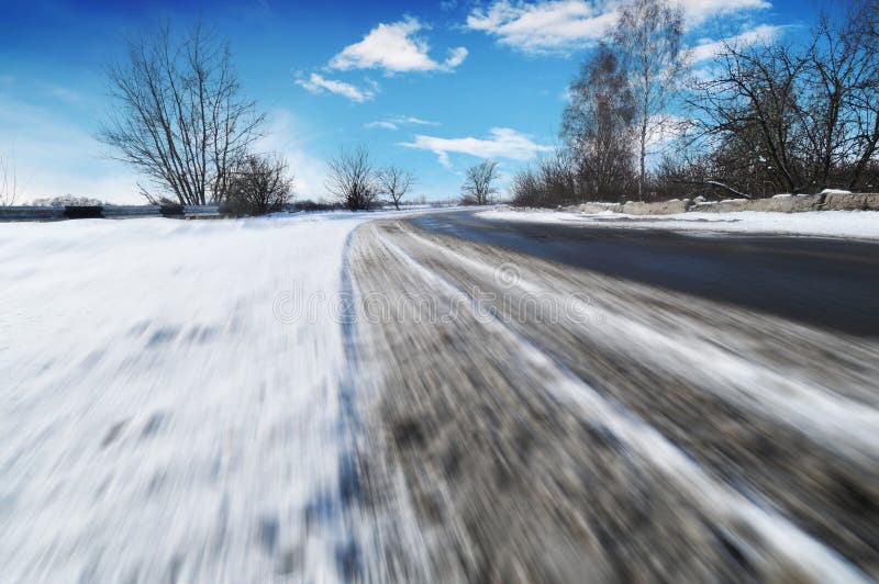 Spår av bildäck på väg i rörelse täckta av vit snö mot blå himmel med moln royaltyfri bild Spår av bildäck på väg i rörelse täckta av vit snö mot blå himmel med moln royaltyfri bild