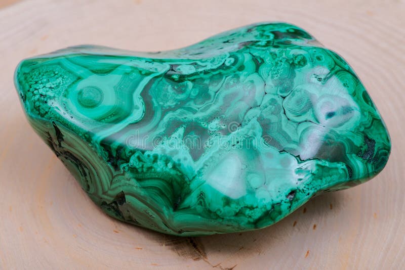 Polished green free form Bullseye Malachite specimen isolated on natural wooden background. Polished green free form Bullseye Malachite specimen isolated on natural wooden background.