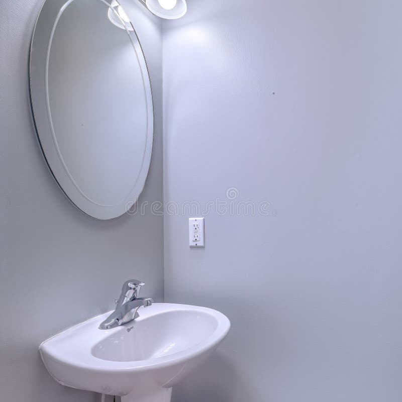 Square Bathroom interior with wall light and oval mirror over stand alone pedestal sink stock photography