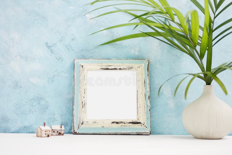 Square blue Photo frame mock up with green tropical plants in vaseand small wooden houses on shelf. Scandinavian style stock photography